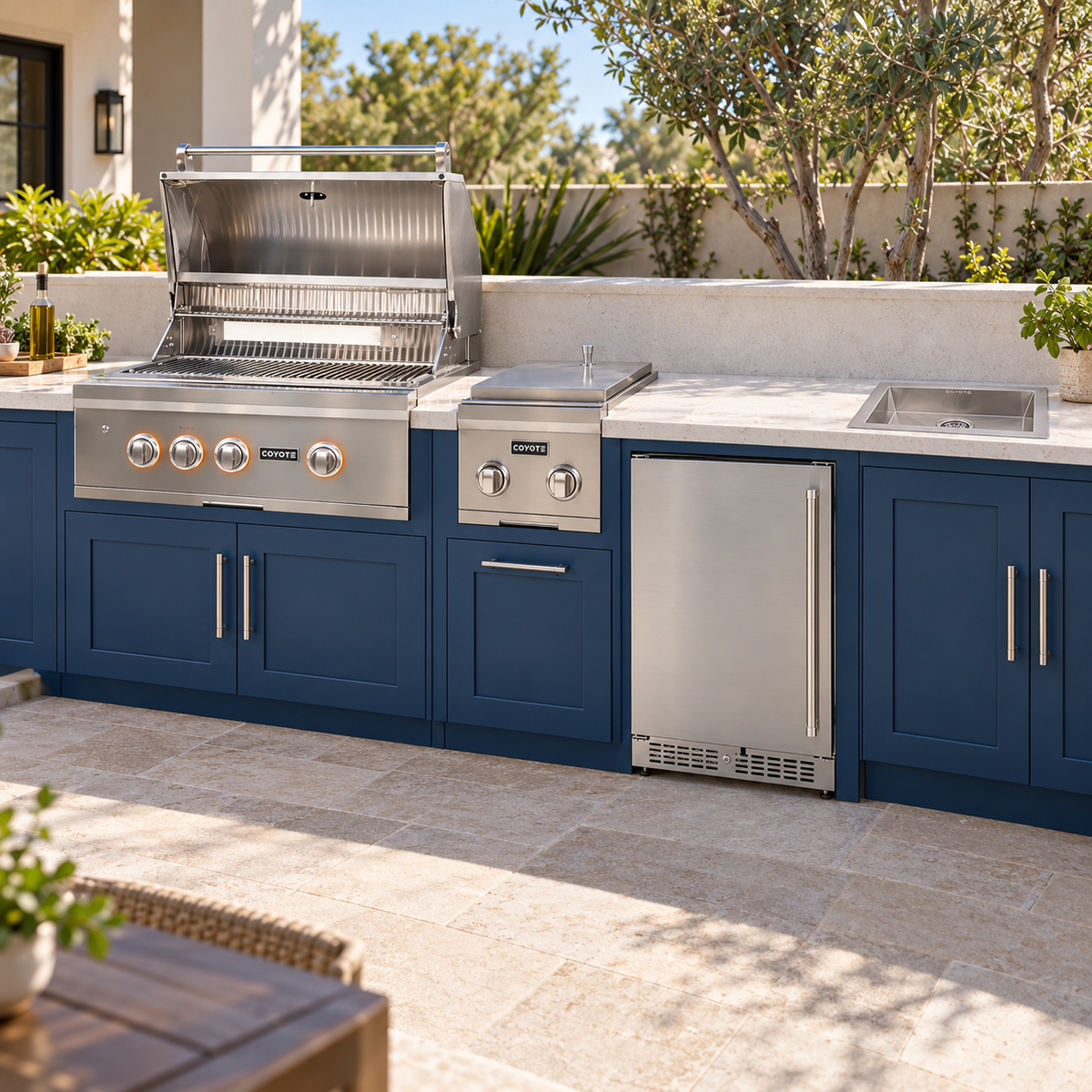Coyote Weekend Host Package – 30" Grill, 24" Refrigerator, Double Side Burner & Drop-In Sink installed in an outdoor kitchen; cabinetry and setting shown for inspiration